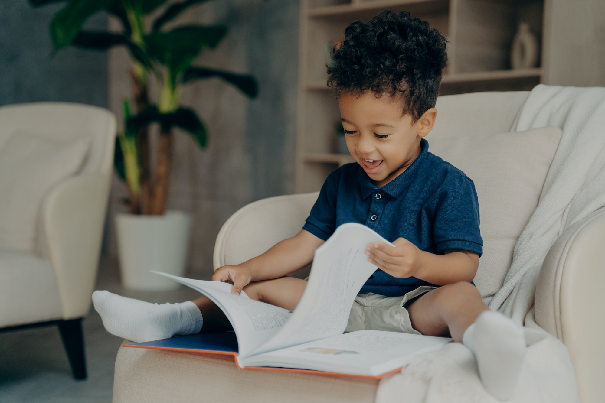 Happy mixed race little kid with cute curly hair reading book at home
